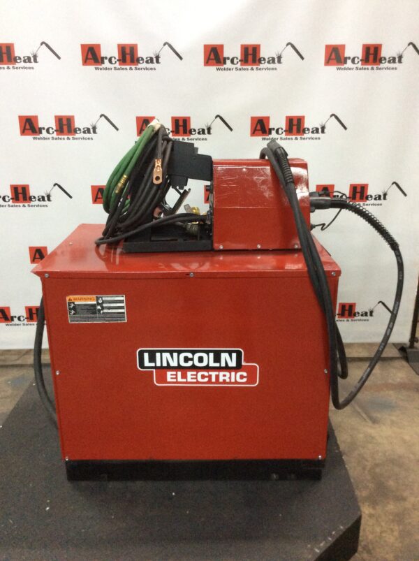 A red lincoln electric welding machine sitting on top of a floor.