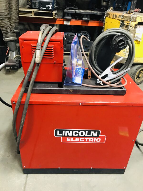 A red lincoln electric welding machine with wires and a blue tank.